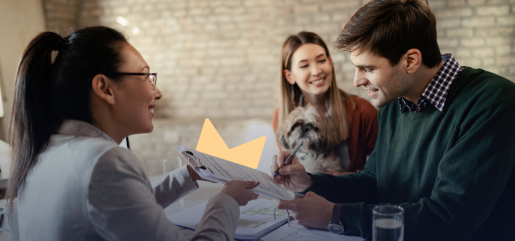 One person holding a clipboard with a piece of paper on it so that another person can sign the paper while a third person smiles at the signer.