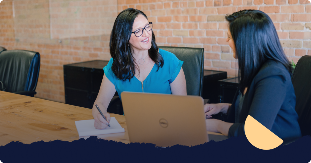 A person is writing on a notepad with questions to ask potential tenants while another person sits beside them with an open laptop.