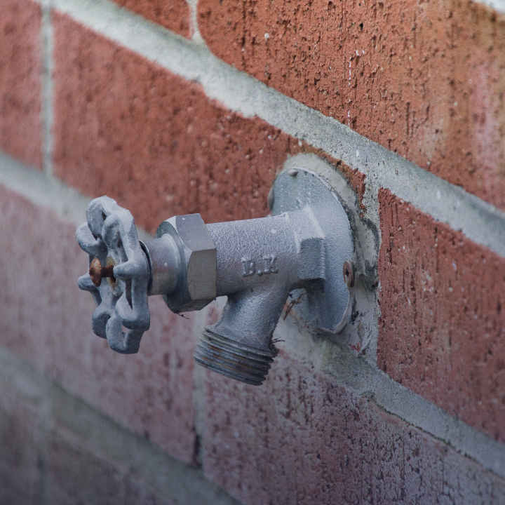 An exterior faucet mounted to a brick wall