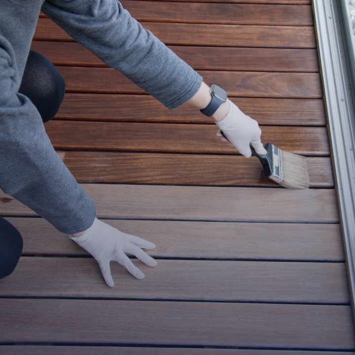 A person with gloves on who is staining an outdoor wooden deck with a brush