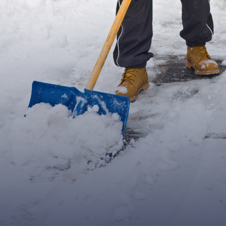 A person wearing boots and shoveling snow