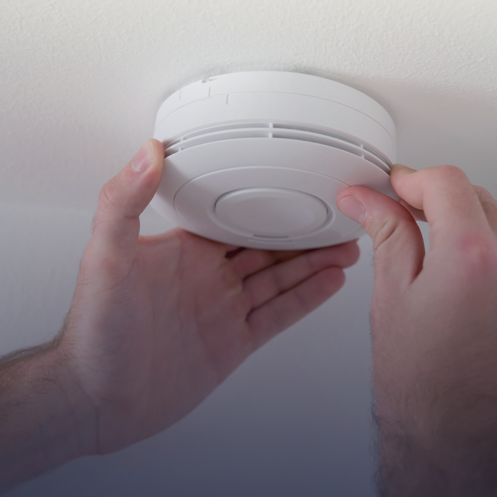 A person adjusting a smoke detector that is mounted on the ceiling