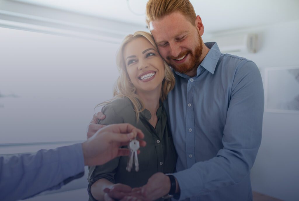 Couple embracing one another and getting house keys handed to them