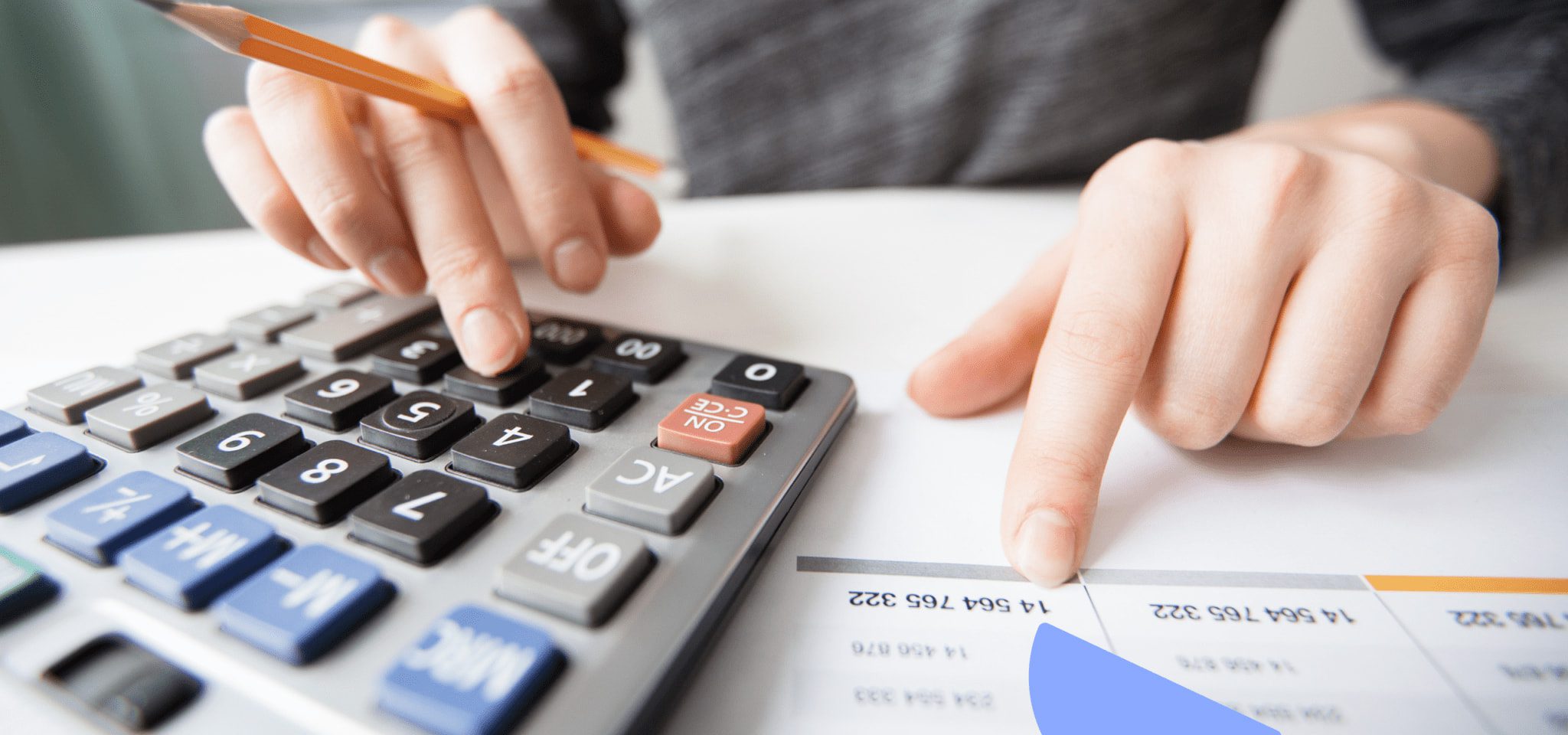 This is a close-up of a pair of hands on a desk. One hand is holding a pencil and resting on a calculator. The other hand is pointing to a number on a piece of paper.