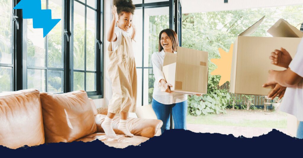 Asian woman holding a moving box and her young daughter jumping on the couch