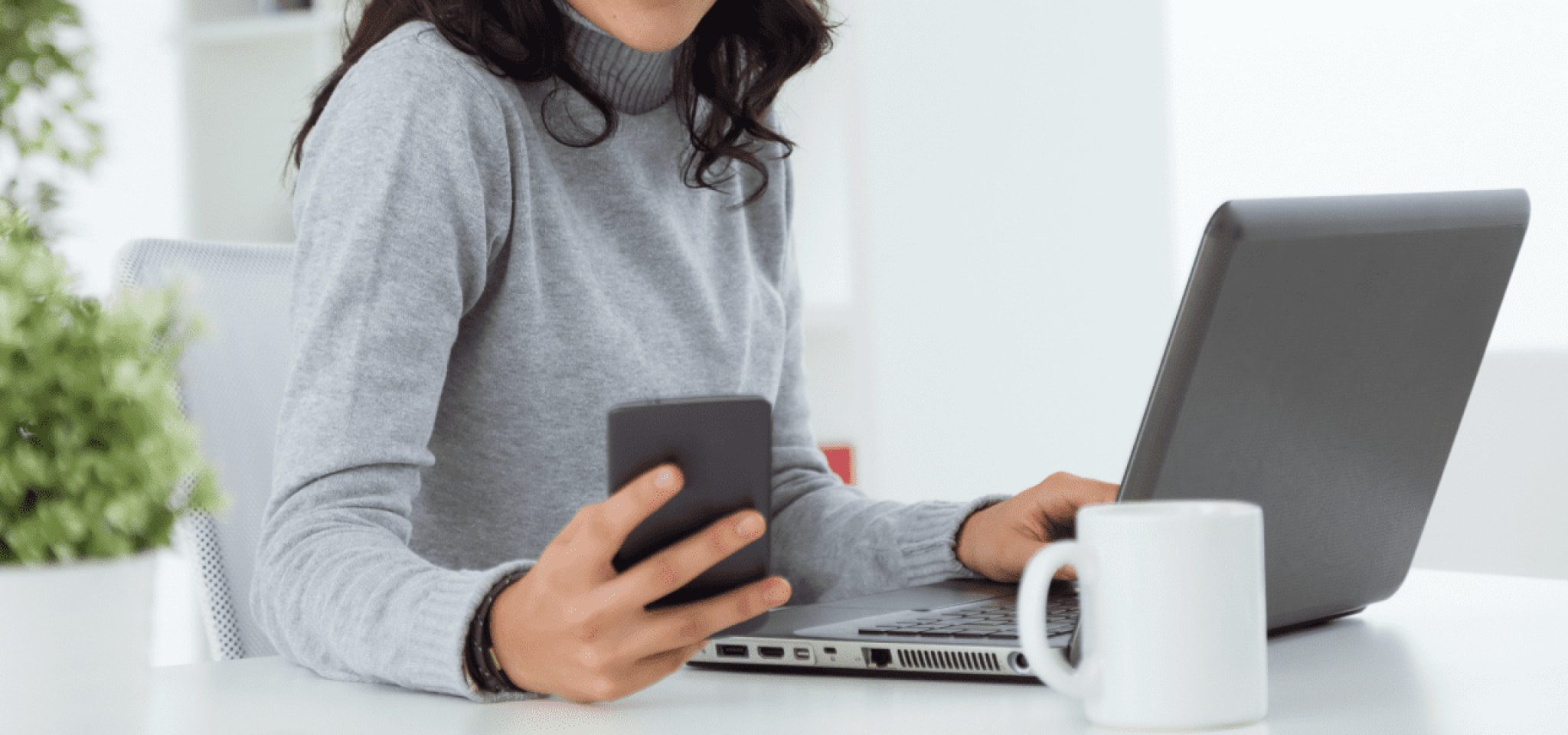 A person holding a cell phone in their right hand, and their left hand on a laptop